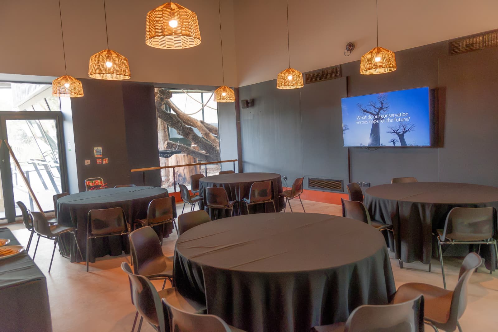 A conference room with round tables, black tablecloths, hanging lights, a large window, and a screen displaying a conservation-related question.