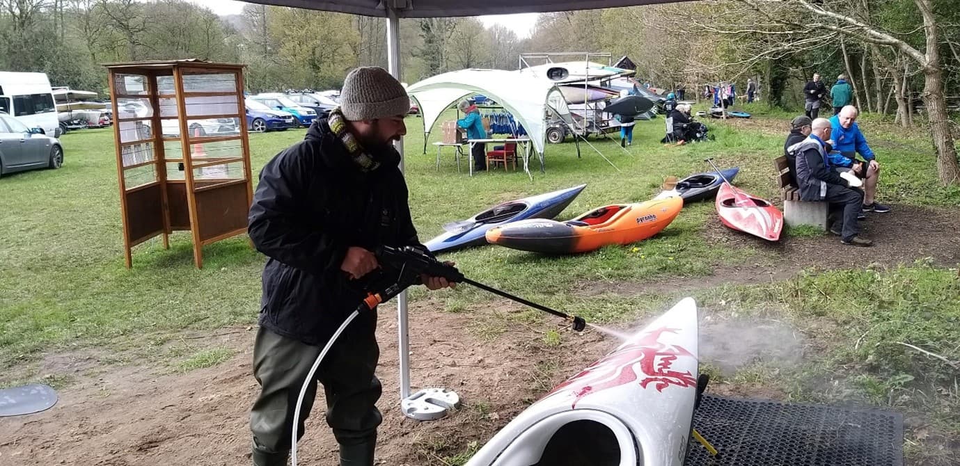 A man holding a jetwash and spraying down a canoe