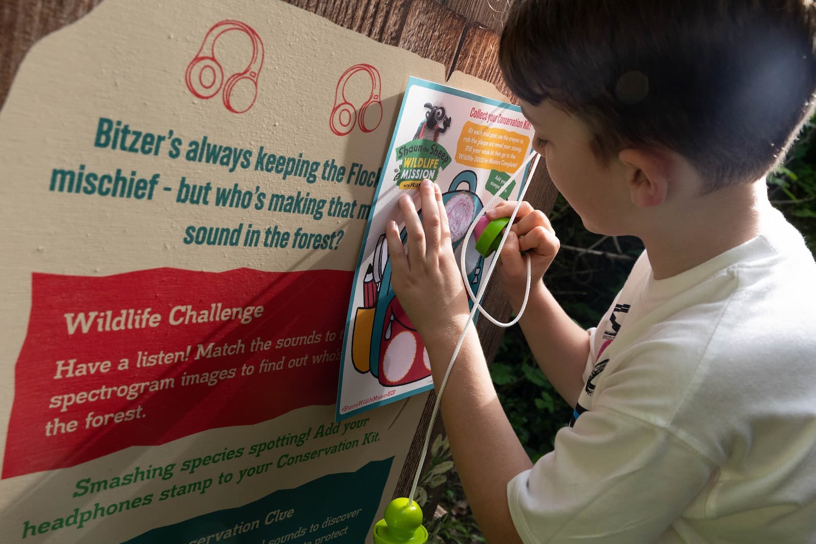 A child interacts with a Shaun the Sheep Wildlife Mission display, listening through headphones and following a wildlife challenge on a sign.